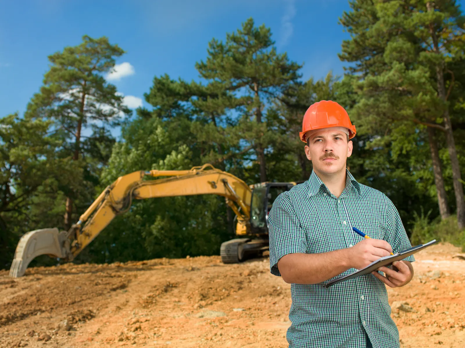 Construction operator holding fuel log sheet with excavator in background